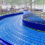 An empty blue conveyor belt with a plastic blue protection fence along the edge, inside a large warehouse.