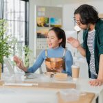 Two people gather around a table discussing something. Various types of packaging surround the table in front of them.