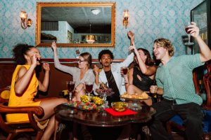 A group of friends seated at a restaurant table all holding their adult beverages in the air for a "cheers!"