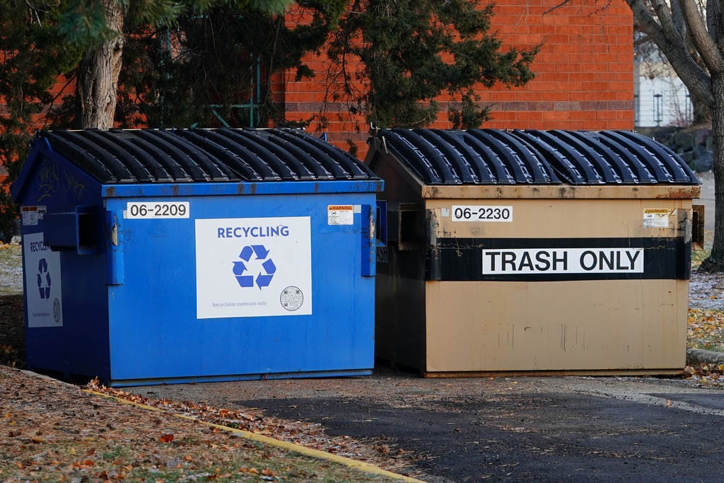 Two large commercial waste hoppers sit side-by-side in the business parking lot. One is for recycle and one is for trash.