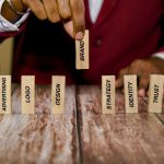 A person in a red sweater sits at the table lifting up a wooden block that says "brand." Other wooden blocks sit on the table.