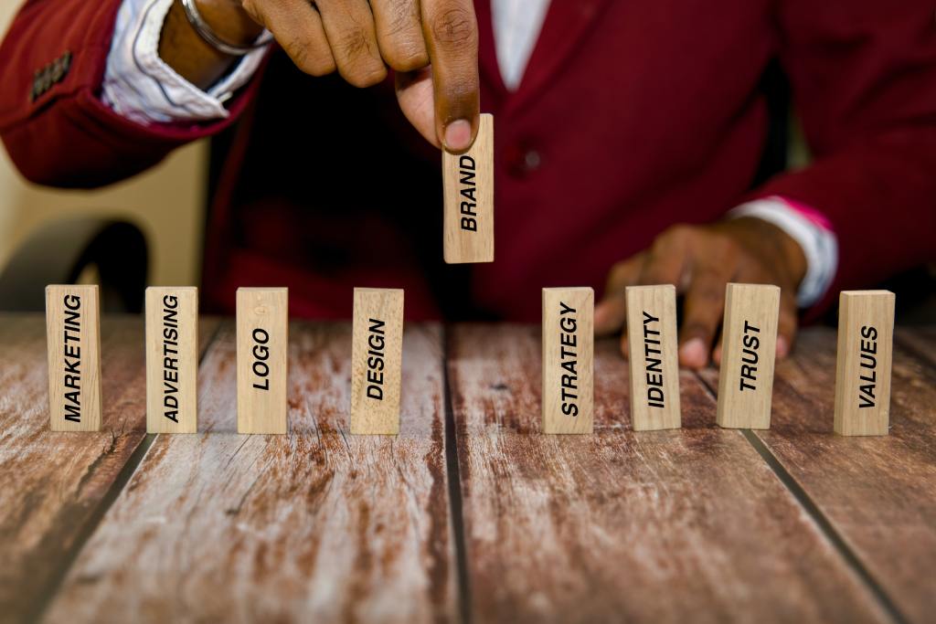 A person in a red sweater sits at the table lifting up a wooden block that says "brand." Other wooden blocks sit on the table.