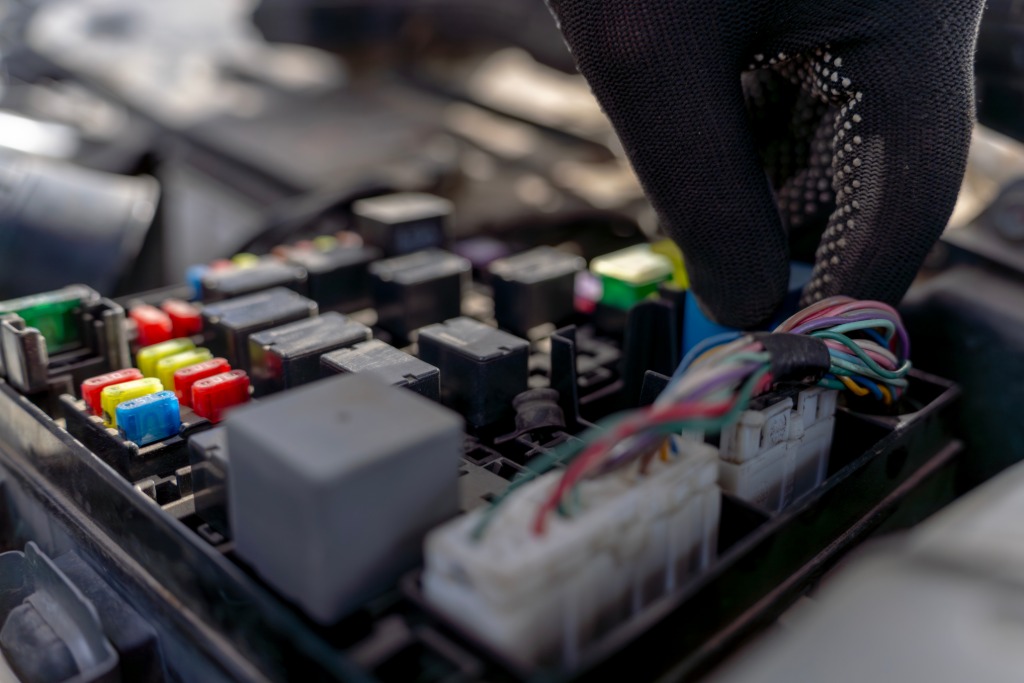A close-up view shows a person wearing black work gloves is working on colorful automotive wires.