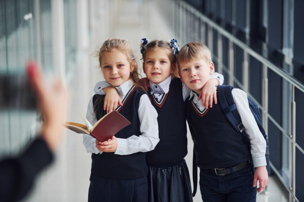 Three students standing in a school hallway. A person stands in front of the students to take a photo.