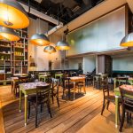 The interior of a restaurant with large hanging pendant lights above tables that seat two to four guests.