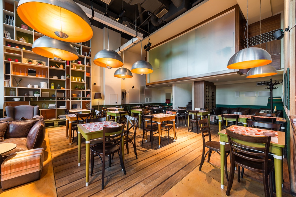 The interior of a restaurant with large hanging pendant lights above tables that seat two to four guests.