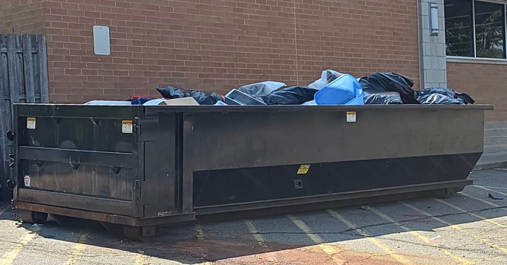 A large dumpster sits outside a commercial business. The dumpster is full of waste from business operations.