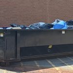 A large dumpster sits outside a commercial business. The dumpster is full of waste from business operations.