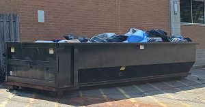 A large dumpster sits outside a commercial business. The dumpster is full of waste from business operations.