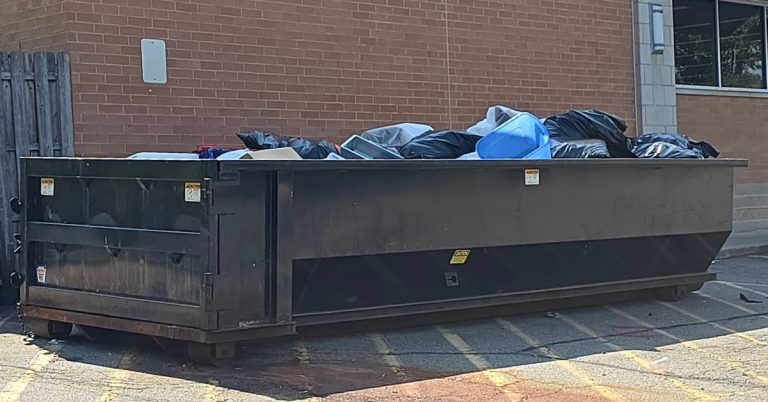 A large dumpster sits outside a commercial business. The dumpster is full of waste from business operations.