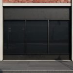 A storefront with dark glass windows, red brick above, light walls, a sidewalk, and shadows across the facade.